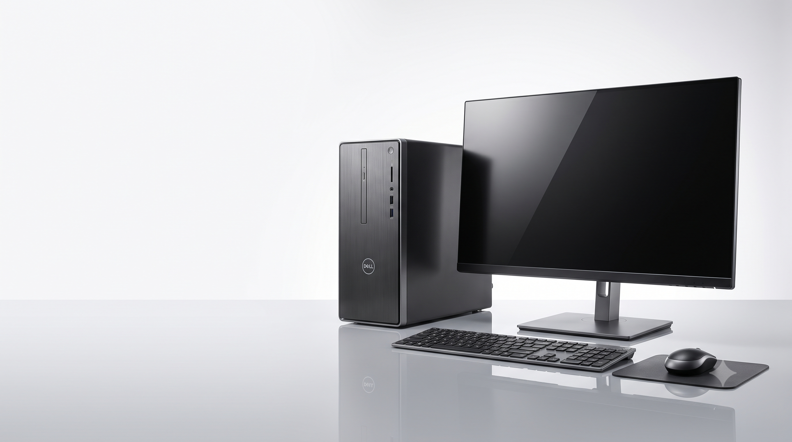A Dell desktop computer setup on a reflective light gray surface, featuring a black tower PC, external monitor, keyboard, and mouse on a mouse pad against a clean white studio background.